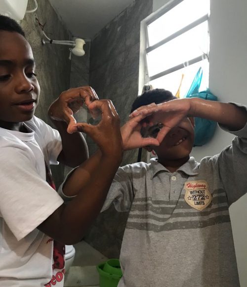 EduMais after-school program students Andre and Romulo form heart shapes with their hands