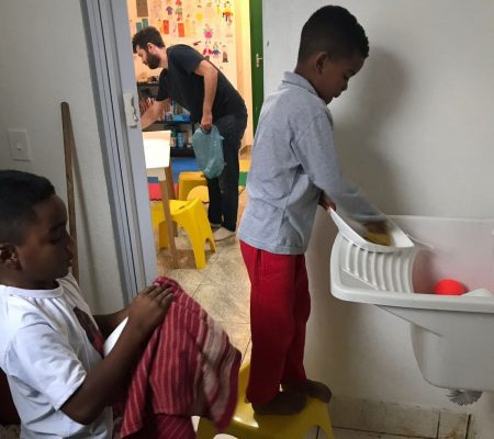 EduMais after-school students wash up their plates while volunteer Ed tidies the room in the background