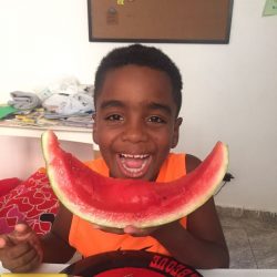 EduMais after-school program student Andre grins widely with an eaten segment of a watermelon