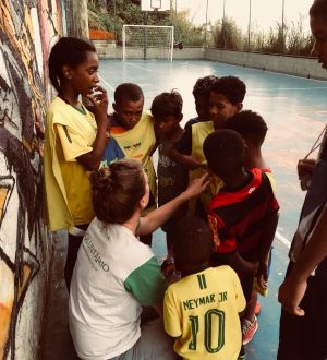 EduMais volunteer Iris squats down to talk with the students on the football program who surround her