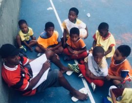 EduMais Football Program leader William sits on the soccer pitch and takes the register as the kids arrive to train