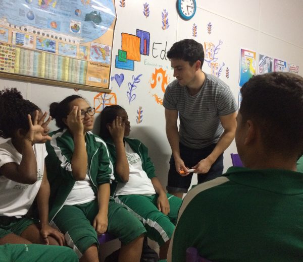 EduMais volunteer teacher Donal in the classroom with three EduMais girl students who hold their hands to their heads