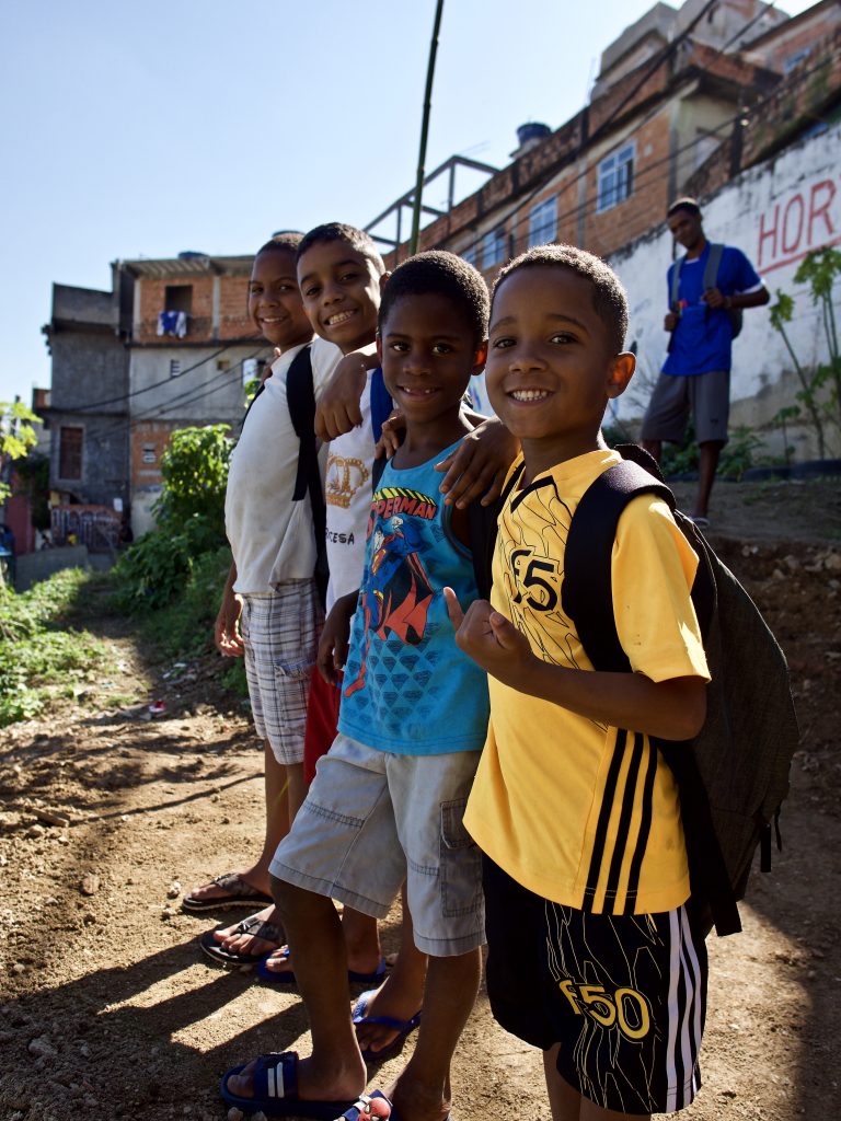 4 students on EduMais's Soccer Programs smile in the favela with their donated backpacks from WINGS Foundation