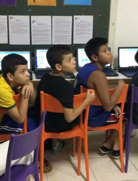 Four boys on EduMais's Programming Camp in front of their computers and with volunteer Audrey looking at whiteboard