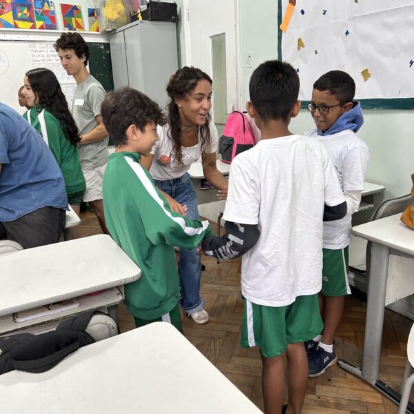 A volunteer smiling and engaging with a group of children in a classroom, as they stand in a circle holding hands during an activity