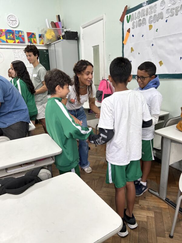 A volunteer smiling and engaging with a group of children in a classroom, as they stand in a circle holding hands during an activity