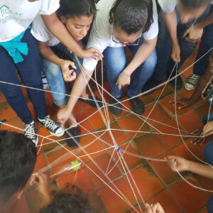 Collaboration value home page A group of students in Rio de Janeiro’s favela working together to lift a plastic bottle with cords during an EduMais class, building problem-solving skills and empowerment through teamwork.
